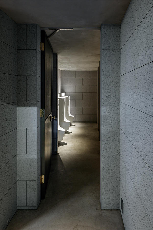 研究開発棟1階男子トイレを前室から見る。INAXの自動洗浄センサー付き小便器。照度や素材のカラートーンを抑え、落ち着いた上質な空間としている