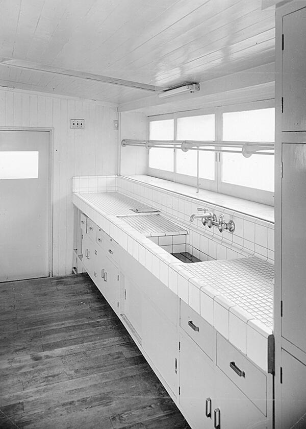 1950年頃、東京都内に建てられた個人邸の台所。大きさの異なる正方形や入隅、出隅、見切り、笠木など、さまざまな形状の白色タイルを用い、シンクと天板、水切りを細やかに美しく納めている。写真提供：INAXライブミュージアム