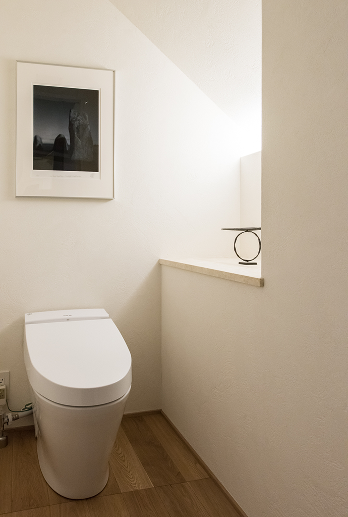 1階トイレ、階段の下になっている、天井の低いところにカウンターを設けてアートが置かれている。1階のトイレ「SATIS Sタイプ/ピュアホワイト」